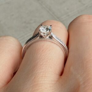Close-up of a diamond engagement ring on a finger, with a large central stone held by prongs and a double-band setting.
