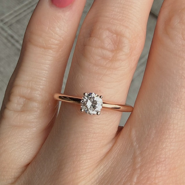 Rose gold solitaire diamond ring on a finger, close-up view highlighting the band and diamond setting.