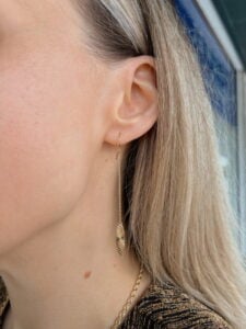 Close-up of a woman's ear wearing a long gold threader earring with a leaf pendant.