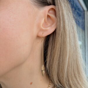 Close-up of a woman's ear wearing a long gold threader earring with a leaf pendant.
