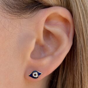 Close-up of an ear wearing a blue eye-shaped stud earring with a gold rim on the earlobe.