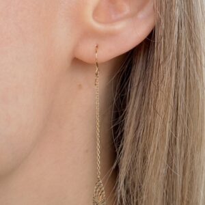 Close-up of a woman's ear with a long gold chain earring featuring a leaf-shaped pendant.
