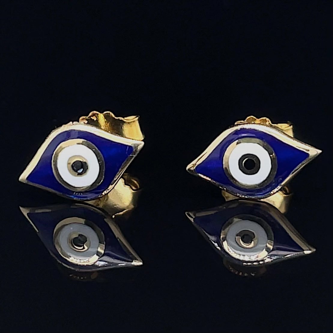 Pair of gold cufflinks with blue enamel and an eye motif, set on a reflective black surface