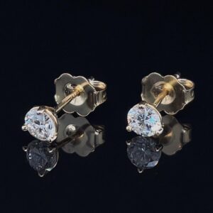 Pair of diamond stud earrings with yellow-gold settings on a black reflective surface.