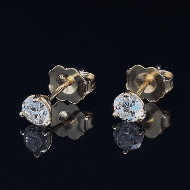 Pair of diamond stud earrings with yellow-gold settings on a black reflective surface.