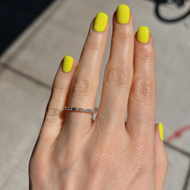 Close-up of a hand with neon yellow manicure and a diamond-studded ring on the ring finger in bright outdoor light.