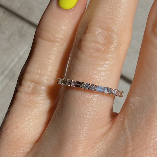 Rose gold ring with evenly spaced square-cut diamonds on a finger in bright light.