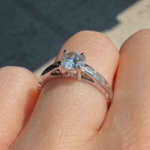 Diamond solitaire engagement ring on a finger with an engraved band and prong setting.