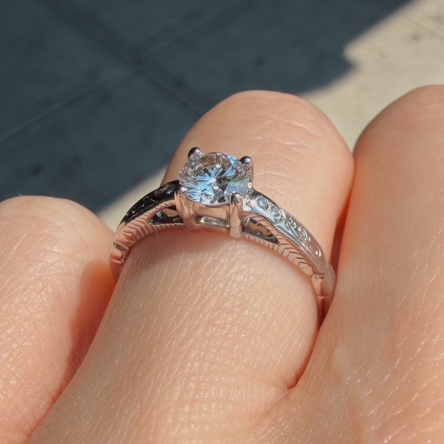 Diamond solitaire engagement ring on a finger with an engraved band and prong setting.