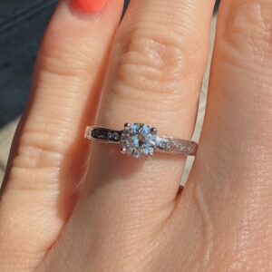 Engagement ring with a round-cut diamond center and engraved band on a finger