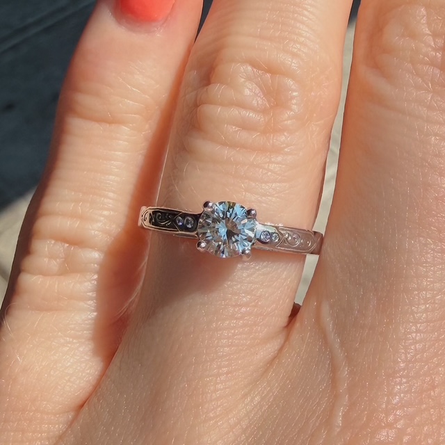 Engagement ring with a round-cut diamond center and engraved band on a finger