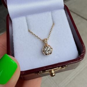 Diamond pendant necklace in a burgundy jewelry box with white interior, showcasing a round-cut stone on a delicate gold chain.