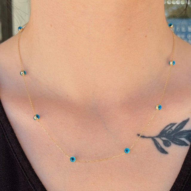 Gold chain necklace with blue beads draped around a woman's neck, with a leaf tattoo visible on the chest area.