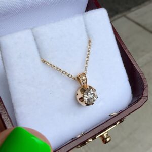 Gold pendant necklace with a round diamond in a white velvet jewelry box.
