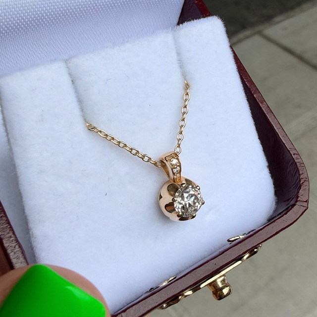Gold pendant necklace with a round diamond in a white velvet jewelry box.