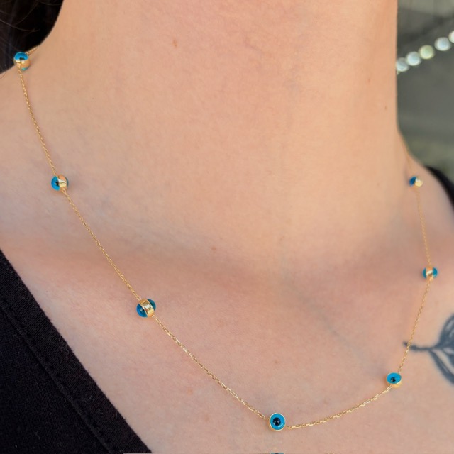 Delicate gold chain necklace with small blue evil-eye beads along the neckline.