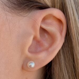 Close-up of a human ear with a pearl stud earring on the earlobe.