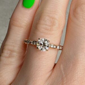 Rose gold ring with a large round-cut diamond solitaire and small diamonds along the band, worn on a finger with a neon-green nail.