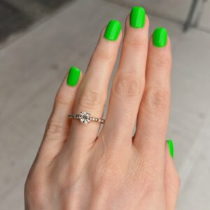 Hand with neon green nails wearing a diamond engagement ring on the ring finger of a left hand.