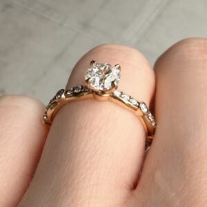 Close-up of a rose-gold engagement ring with a large round-cut diamond in a prong setting, worn on the finger with a diamond-studded band visible nearby.