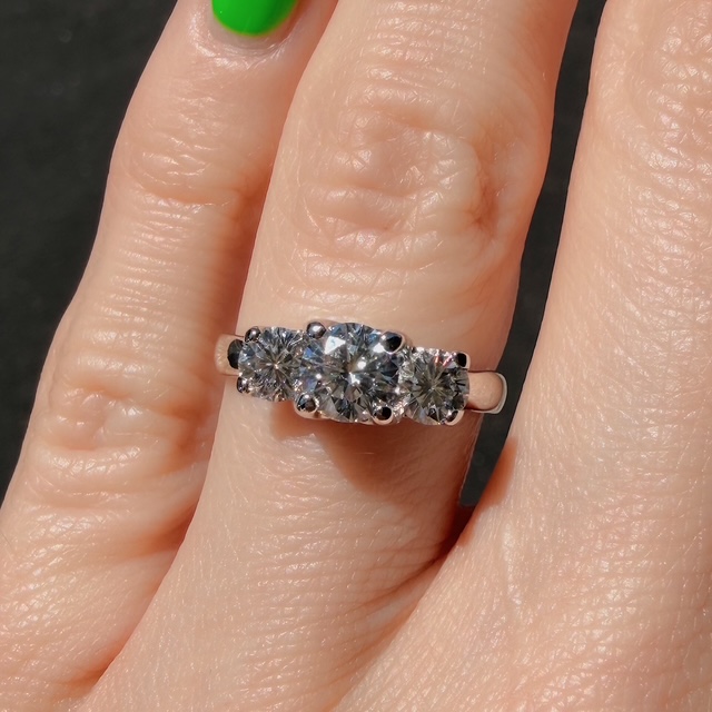 Silver ring with three round-cut diamonds on a finger with green nail polish.