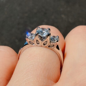 Close-up of a rose-gold ring with a large central diamond and two side stones held by prongs, on a fingertip.