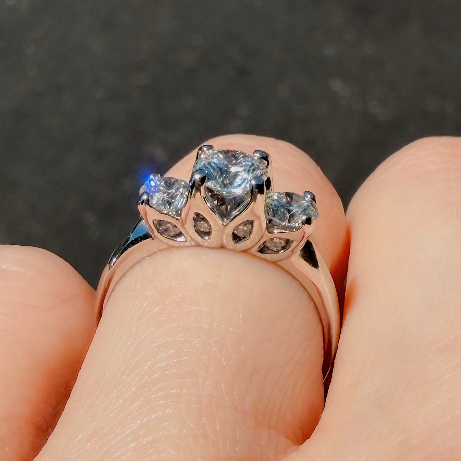 Close-up of a rose-gold ring with a large central diamond and two side stones held by prongs, on a fingertip.