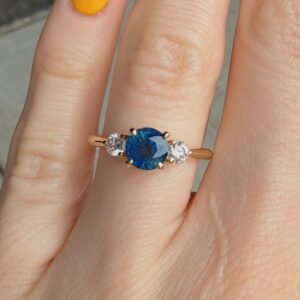 Gold ring with an oval blue sapphire center flanked by two diamonds on a finger