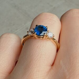 Rose gold ring featuring a blue sapphire center stone flanked by two diamonds on a finger.