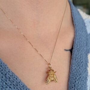Gold bee pendant necklace resting on a collarbone over a blue knit sweater.