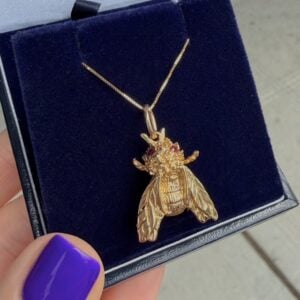 Gold bee pendant necklace with red gemstones, resting in a navy velvet jewelry box.