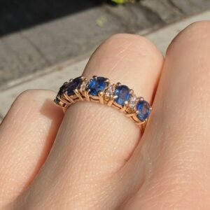 Gold ring with a row of blue sapphires and small diamonds on a finger.