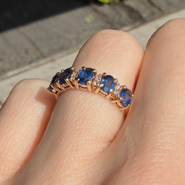 Gold ring with a row of blue sapphires and small diamonds on a finger.