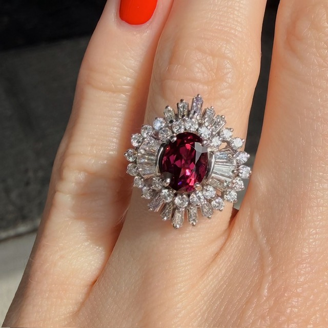 Ring with a large oval red gemstone surrounded by a halo of diamonds on a finger, sparkling jewelry centerpiece.