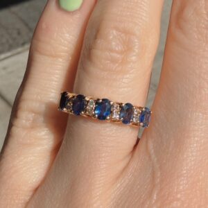 Gold ring with alternating blue stones and small diamonds on a finger (close-up).
