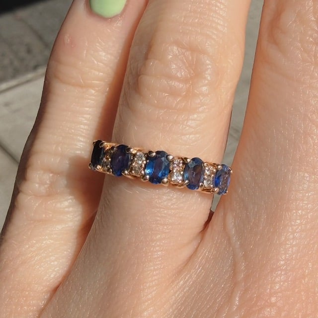 Gold ring with alternating blue stones and small diamonds on a finger (close-up).