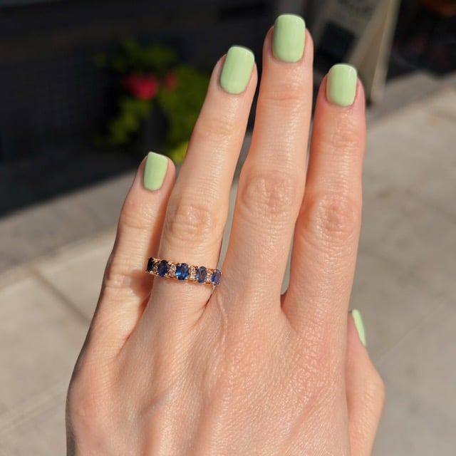 Close-up of a hand with mint-green nails wearing a blue gemstone ring on the ring finger.