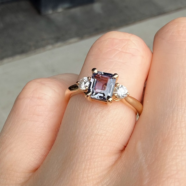Gold ring with a square-cut purple gemstone flanked by two small diamonds on a gold band