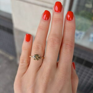 Close-up of a hand with bright red nails wearing a gold solitaire ring with a pale yellow diamond on the ring finger.