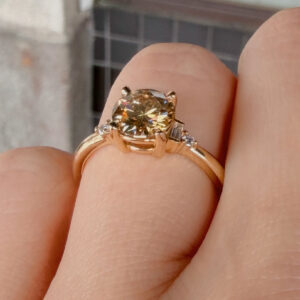 Close-up of a rose-gold ring with a large round-cut diamond on the finger, showcasing brilliance and facets.