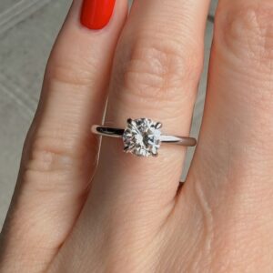 Close-up of a silver solitaire diamond ring on a finger with red nail polish.