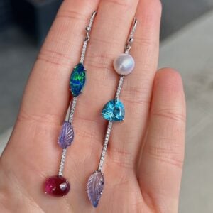 Pair of silver drop earrings with diamond-studded chains; left earring has a green-blue marquise gem, purple leaf charm, and red cabochon, while the right earring has a pearl, blue heart gem, and purple leaf charm.
