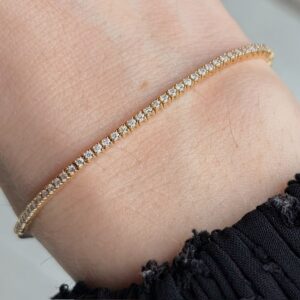 Gold diamond tennis bracelet worn on a wrist, close-up detail of sparkling stones along a thin gold band.