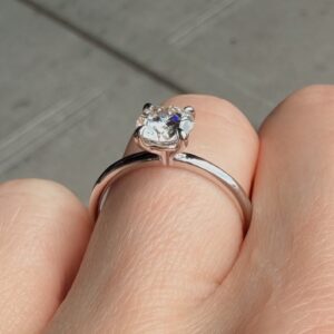 Close-up of a diamond engagement ring with a large cushion-cut diamond held between fingers.