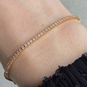 Close-up of a gold diamond tennis bracelet around a light skin wrist, with a black sleeve edge visible nearby.