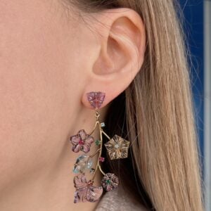 Close-up of a purple floral drop earring on the left ear, with a gold stem and multiple gemstone flowers.