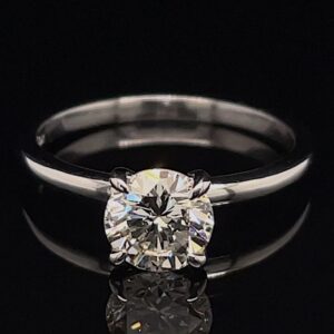 Solitaire diamond ring with a round-cut diamond in a four-prong setting on a black reflective surface.