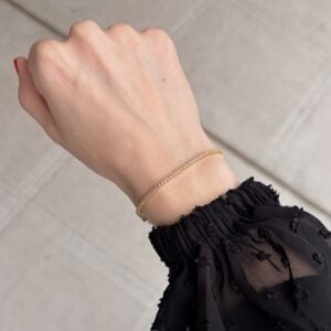Delicate gold bracelet on a woman's wrist, with a sheer black sleeve and light tiled floor in the background.
