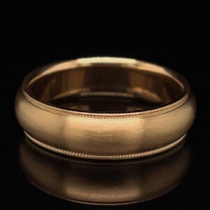 Close-up of a gold wedding band with a delicate beaded edge against a black background