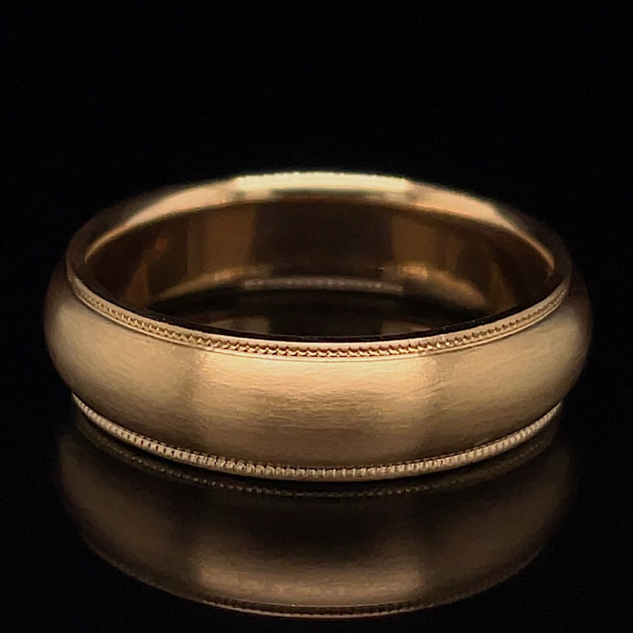Close-up of a gold wedding band with a delicate beaded edge against a black background